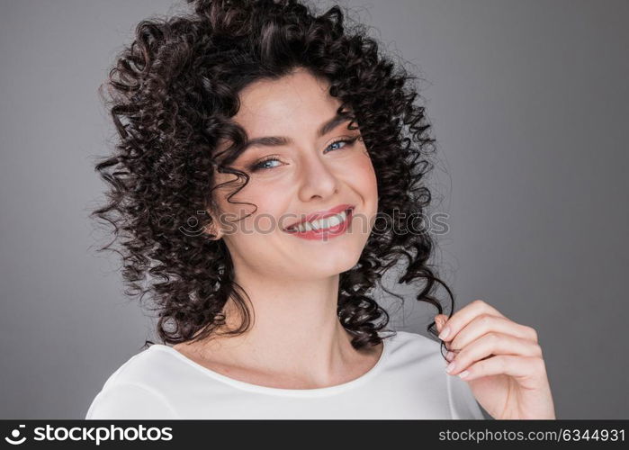 Beautiful woman with curly hair. Portrait of beautiful smiling woman with curly hair, gray background