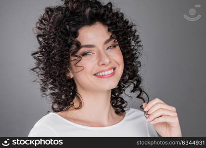 Beautiful woman with curly hair. Portrait of beautiful smiling woman with curly hair, gray background