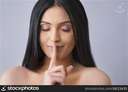Beautiful woman with eyes closed gestures for silence over colored background
