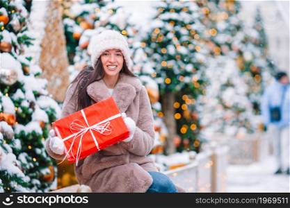 Beautiful woman with gift near Christmas tree in the snow outdoors on a wonderful winter day. Happy girl near fir-tree branch in snow for new year.