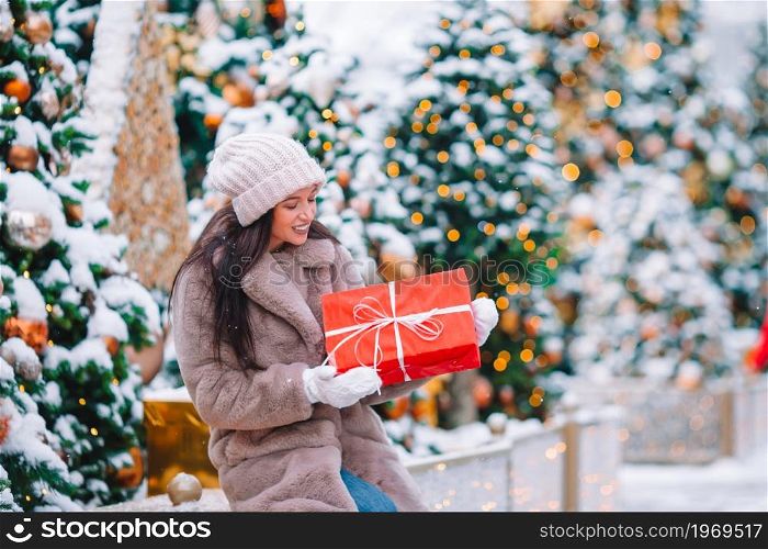 Beautiful woman with gift near Christmas tree in the snow outdoors on a wonderful winter day. Happy girl near fir-tree branch in snow for new year.