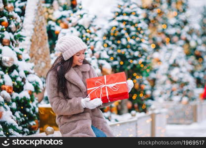 Beautiful woman with gift near Christmas tree in the snow outdoors on a wonderful winter day. Happy girl near fir-tree branch in snow for new year.