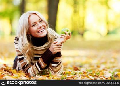 Beautiful woman with green apple in autumn park. Woman with apple