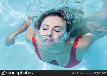 Beautiful woman with her eyes closed emerging from swimming underwater and shooting air bubbles. Leisure concept.. Woman emerging from swimming underwater at the pool