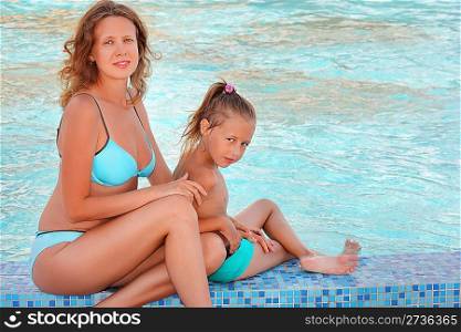 beautiful woman with little girl sit near in pool