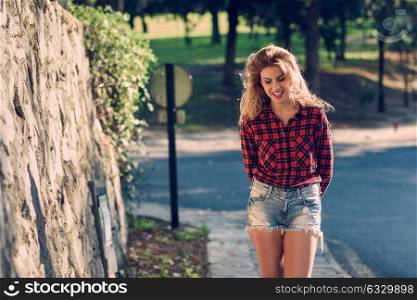 Beautiful woman with long blond curly hair. Enjoyment. Expressive Woman in checkered shirt and blue jeans with toothy Smile