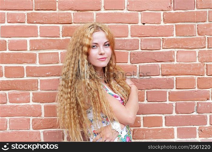 Beautiful woman with long blond hair standing against brick-wall