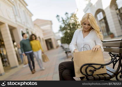 Beautiful woman with paper shopping bag sitting on the bench by the stores