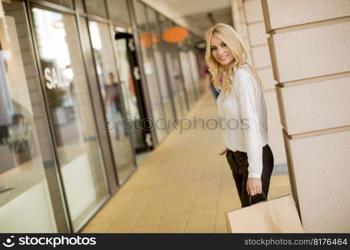 Beautiful woman with paper shopping bag standing by the store