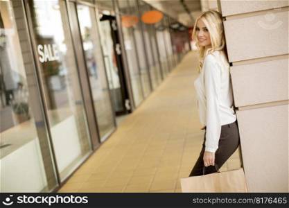 Beautiful woman with paper shopping bag standing by the store