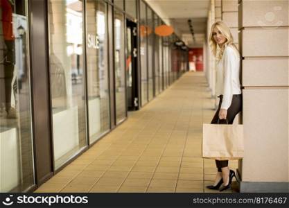 Beautiful woman with paper shopping bag standing by the store