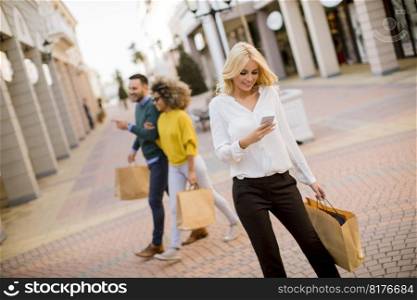 Beautiful woman with paper shopping bag using mobile phone while walking by the stores
