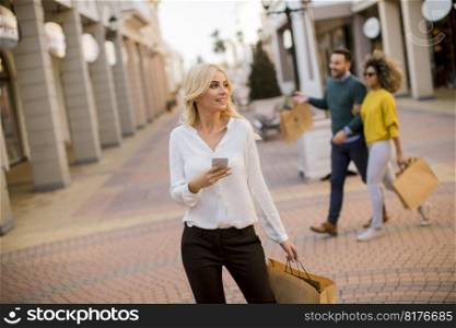 Beautiful woman with paper shopping bag using mobile phone while walking by the stores