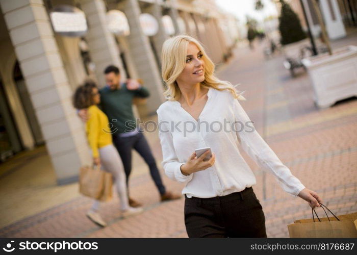 Beautiful woman with paper shopping bag using mobile phone while walking by the stores