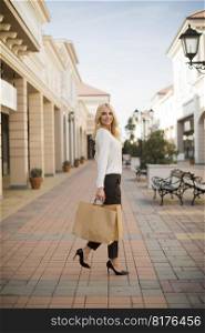 Beautiful woman with paper shopping bag walking by the stores