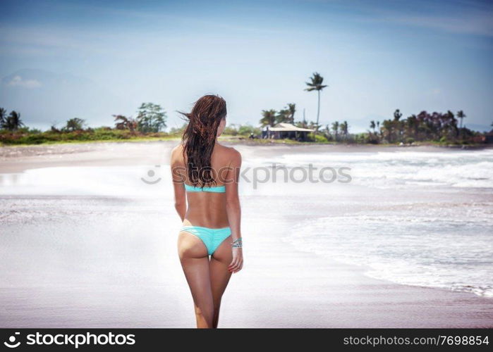 Beautiful woman with perfect body on a beach, walking away along sea coast, summer vacation on a tropical resort