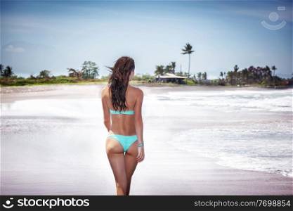 Beautiful woman with perfect body on a beach, walking away along sea coast, summer vacation on a tropical resort