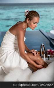 Beautiful woman with pleasure taking bath with foam in the bungalow with open view to the sea, luxury spa resort on Maldives