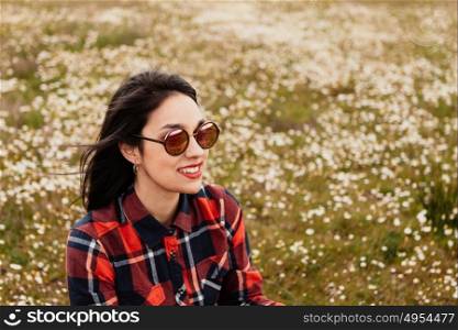 Beautiful woman with sunglasses sitting in the middle of a flowery meadow