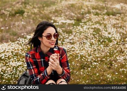 Beautiful woman with sunglasses sitting in the middle of a flowery meadow smelling a daisy
