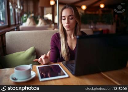 Beautiful woman with tablet pc and laptop work in restaurant. Girl with modern gadget using 4g in restaurant.