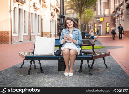 Beautiful woman with tablet relaxing on bench after shopping