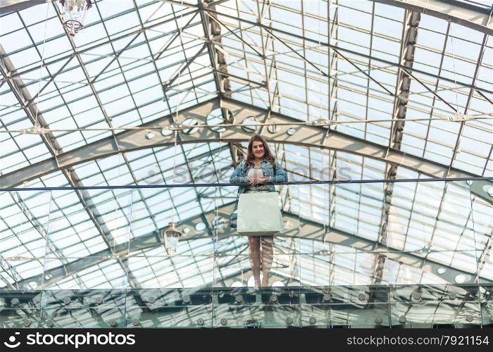 Beautiful woman with white paper bag standing at mall with glass ceiling