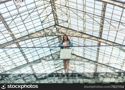 Beautiful woman with white paper bag standing at mall with glass ceiling
