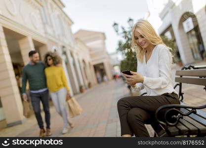 Beautiful woman withmobile phone sitting on the bench by the stores