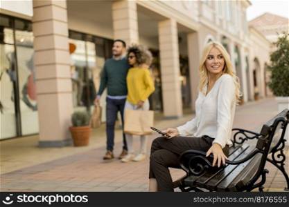 Beautiful woman withmobile phone sitting on the bench by the stores