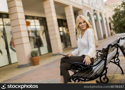 Beautiful woman withmobile phone sitting on the bench by the stores