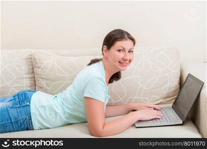 beautiful woman working on a laptop while lying on the couch