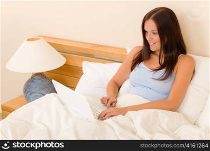 Beautiful woman working on computer lying in white bed