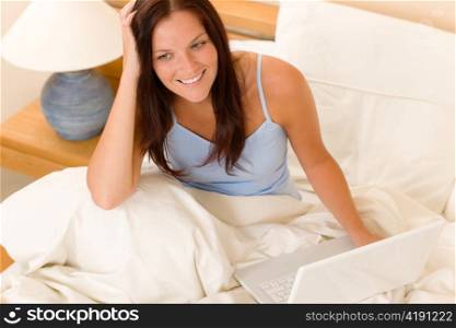 Beautiful woman working on computer lying in white bed
