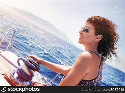 Beautiful woman working on sailboat, holding rope on crank, enjoying bright sunny day, amazing summer adventure on luxury water transport