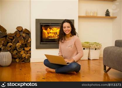 Beautiful woman working with a laptop at the warmth of the fireplace