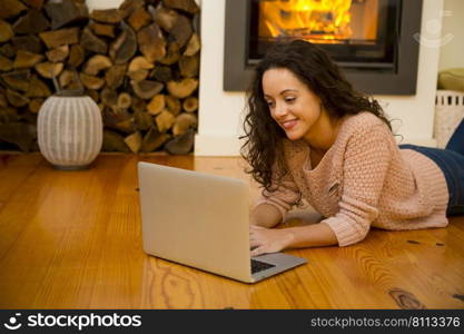 Beautiful woman working with a laptop at the warmth of the fireplace