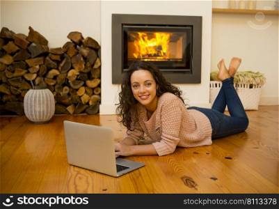 Beautiful woman working with a laptop at the warmth of the fireplace