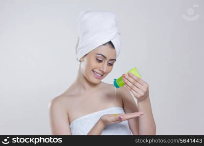 Beautiful woman wrapped in towel pouring beauty product on palm against gray background