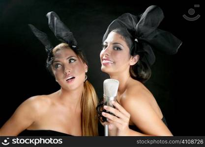 Beautiful women couple singing on a vintage microphone on black background