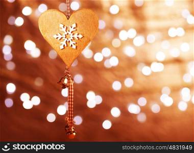 Beautiful wooden heart shaped New Year decoration with snowflake ornament hanging on blur shiny golden background, stylish christmastime bauble