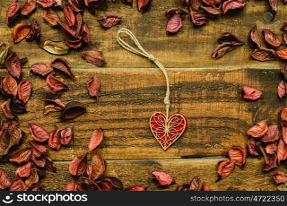 Beautiful wooden heart with red dry petals around on a rustic wood
