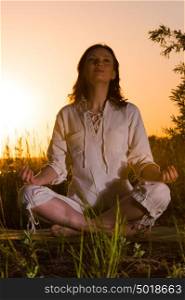 Beautiful Yoga woman siting against sunrise and rays of sun surrounding her