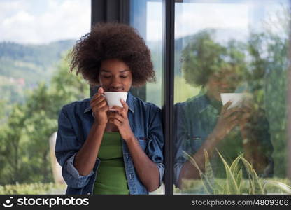 Beautiful young african american woman drinking coffee and looking through a window in her luxury home