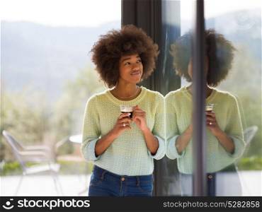 Beautiful young african american woman drinking coffee and looking through a window in her luxury home