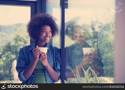 Beautiful young african american woman drinking coffee and looking through a window in her luxury home