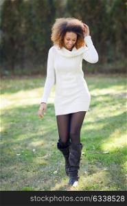 Beautiful young African American woman with afro hairstyle and green eyes wearing white winter dress walking in an urban park