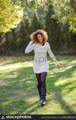 Beautiful young African American woman with afro hairstyle and green eyes wearing white winter dress walking in an urban park