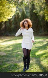 Beautiful young African American woman with afro hairstyle and green eyes wearing white winter dress walking in an urban park