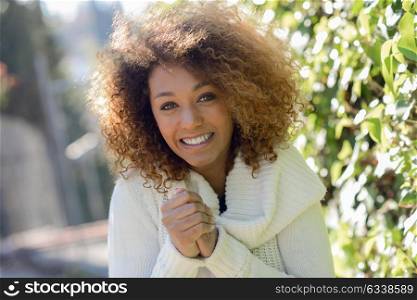 Beautiful young African American woman with afro hairstyle and green eyes wearing white winter dress with cold face